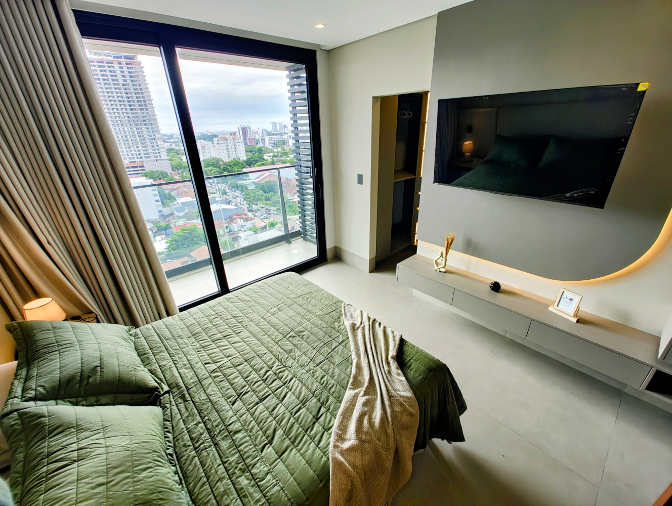 Bedroom area with green bedding, TV wall, and balcony door with city view